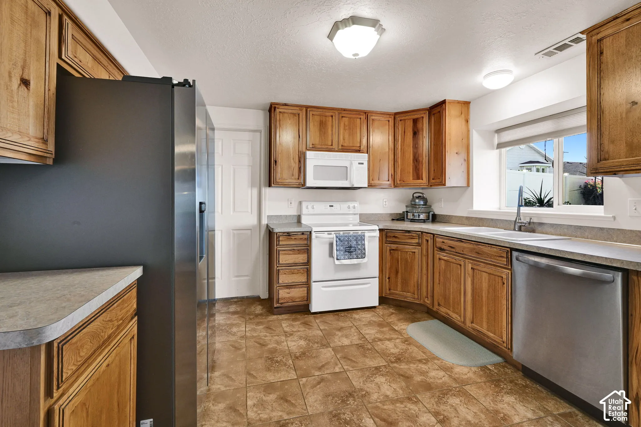 Wood cabinetry with stainless steel appliances, durable countertops, and tiled flooring