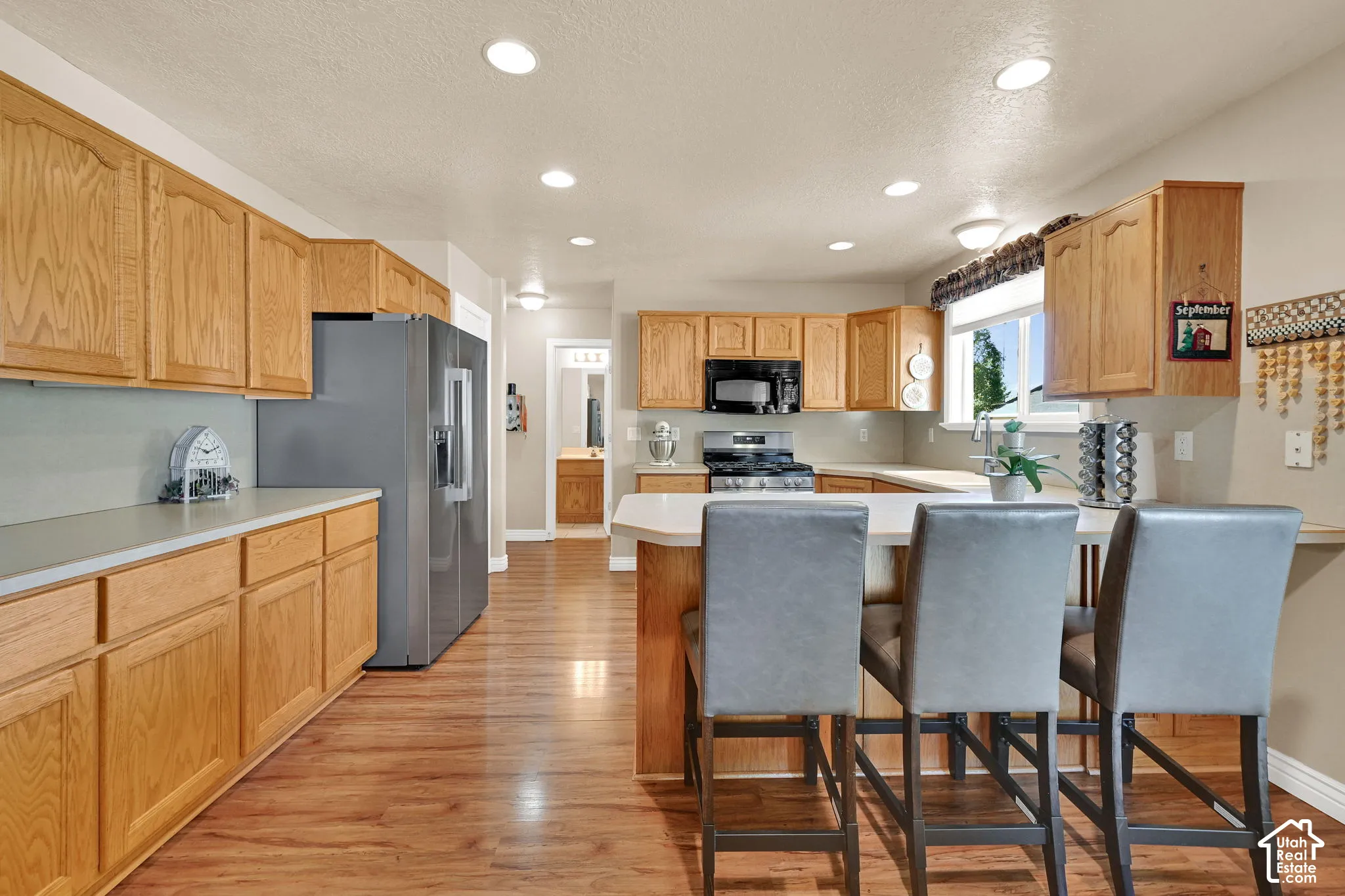 Kitchen featuring wood-finish flooring, recessed lighting, wood cabinetry, stainless steel appliances, and a central island with a breakfast bar