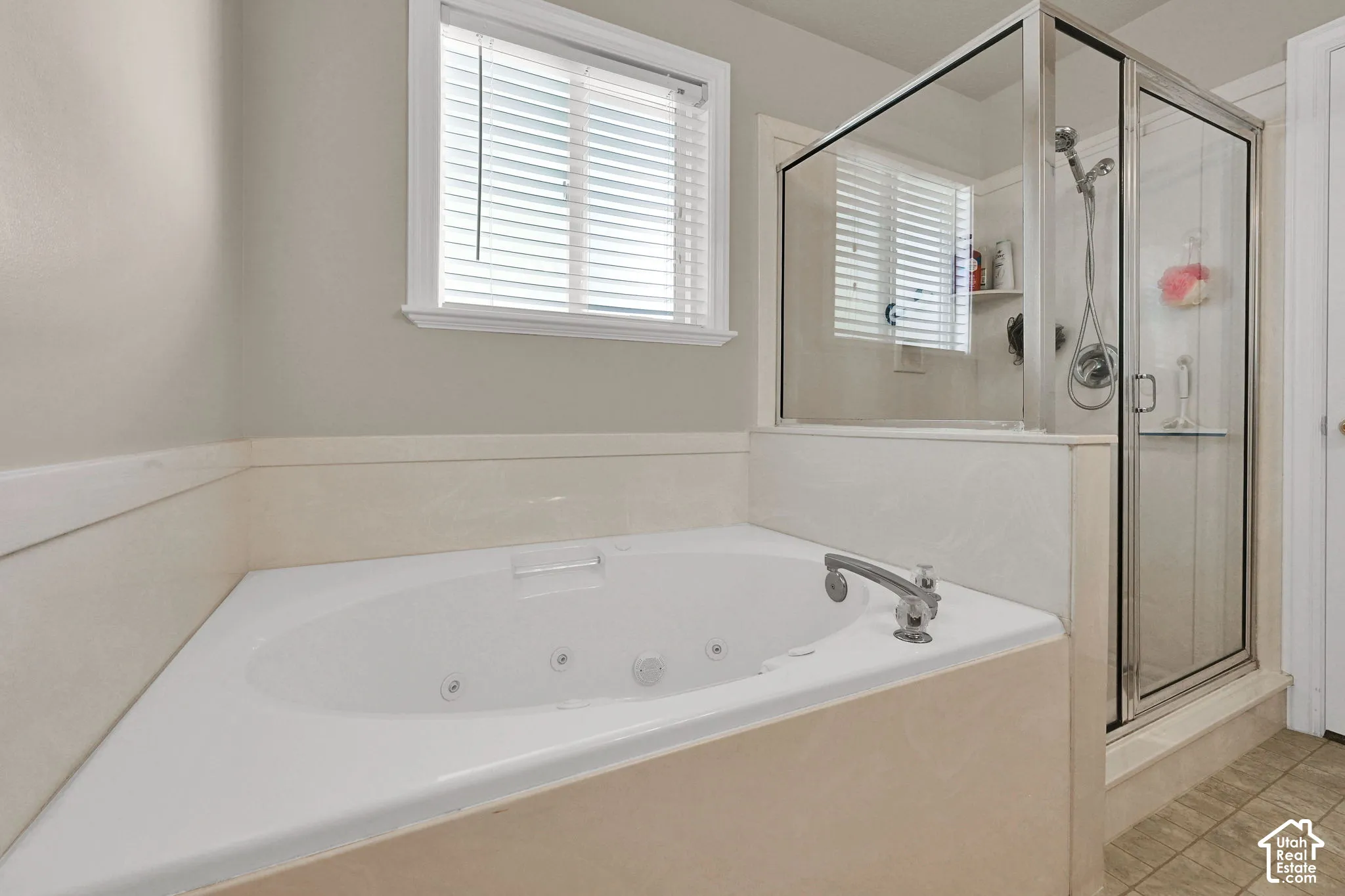 Built-in corner soaking tub with multiple jets, separate glass-enclosed shower, chrome fixtures, and a window with blinds