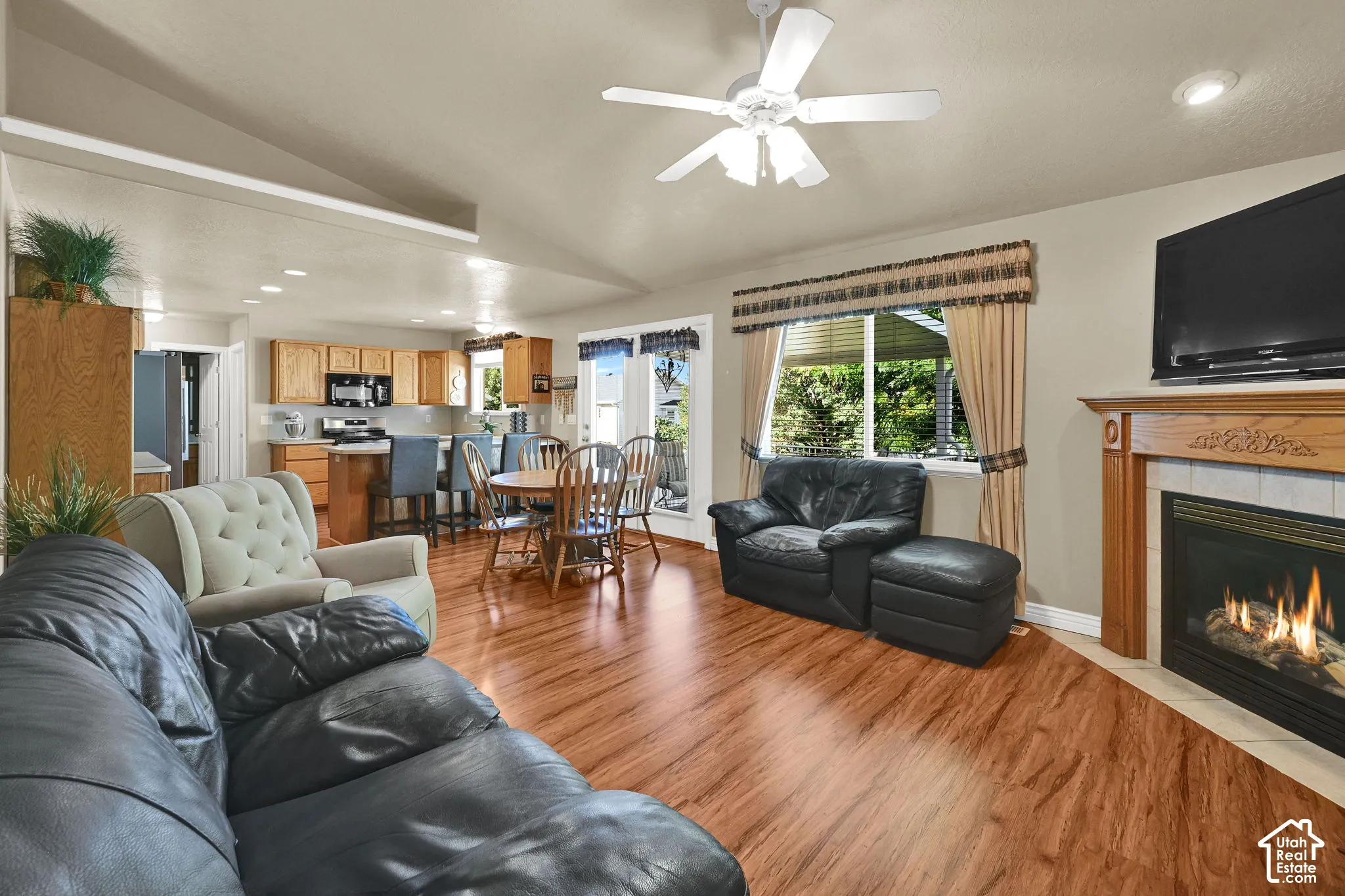 Wood-finish flooring throughout, vaulted ceiling with a ceiling fan, and a gas fireplace with a wood mantel