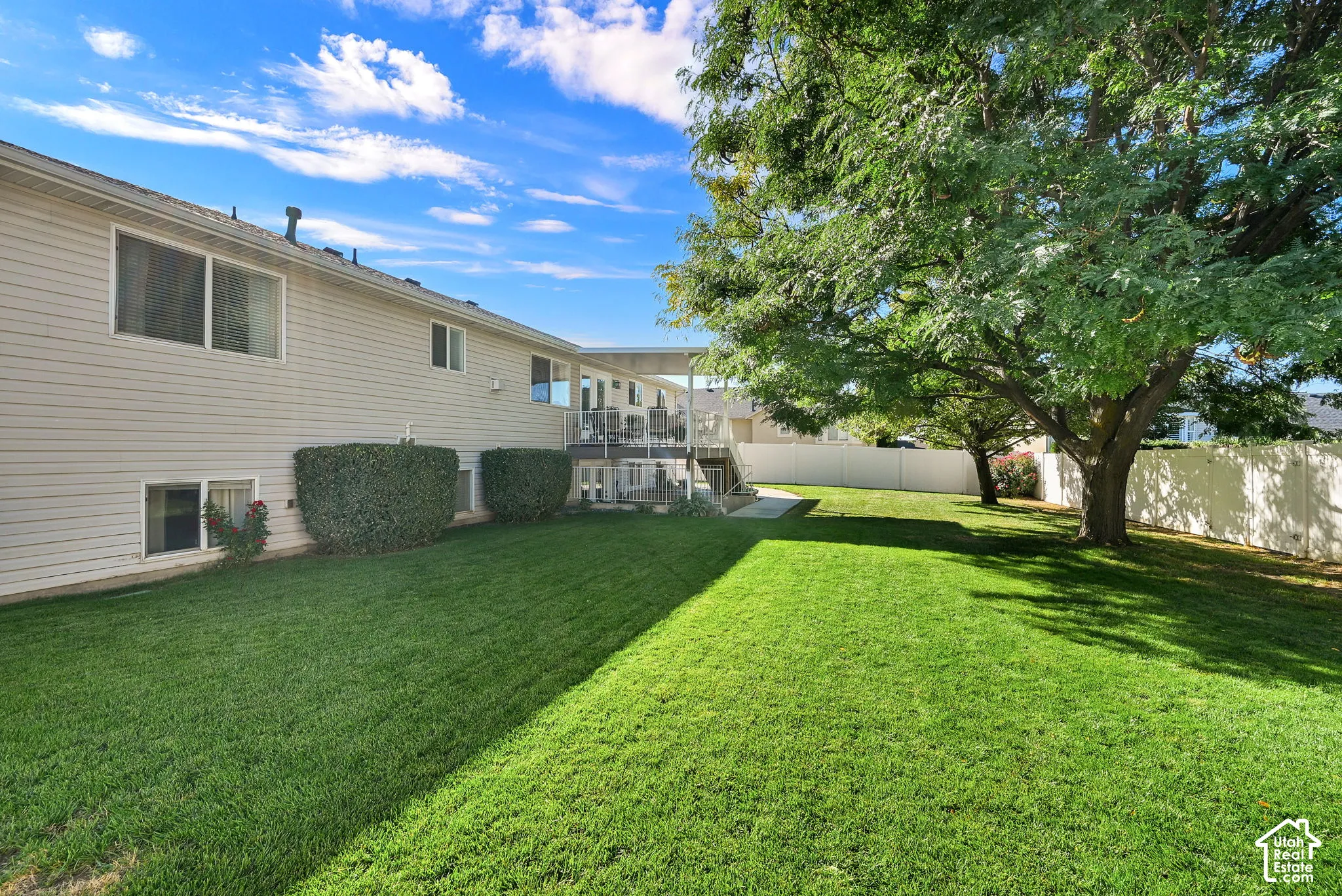 Expansive rear yard featuring green lawn, established trees, privacy fencing, and exterior siding