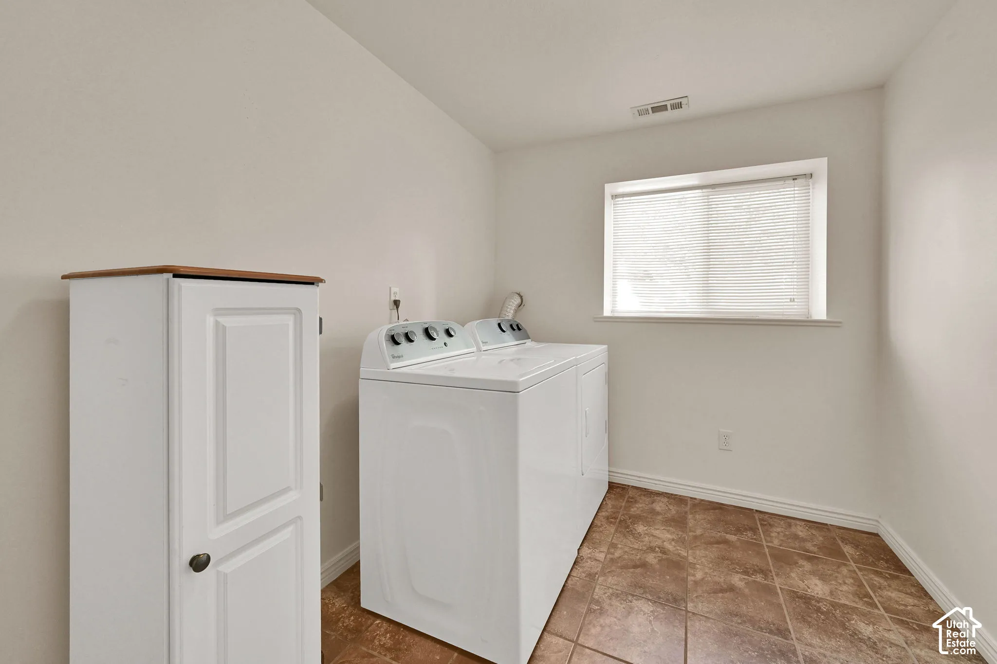 Utility space with tile flooring, a window, and a built-in storage cabinet with a wood-finish top