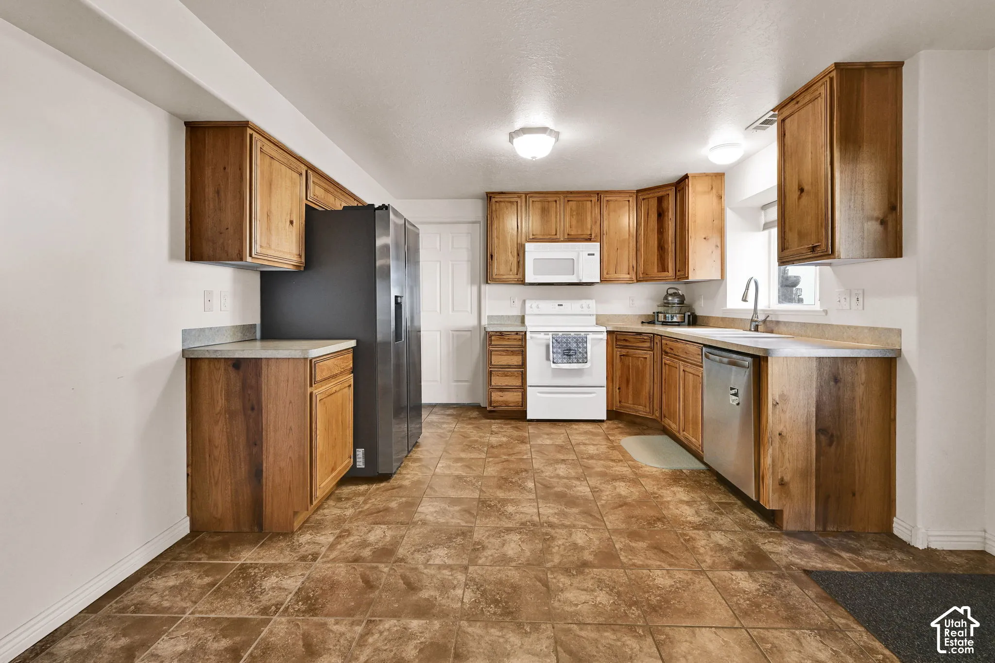 Kitchen featuring wood cabinetry, light-toned countertops, tile flooring, and integrated appliances
