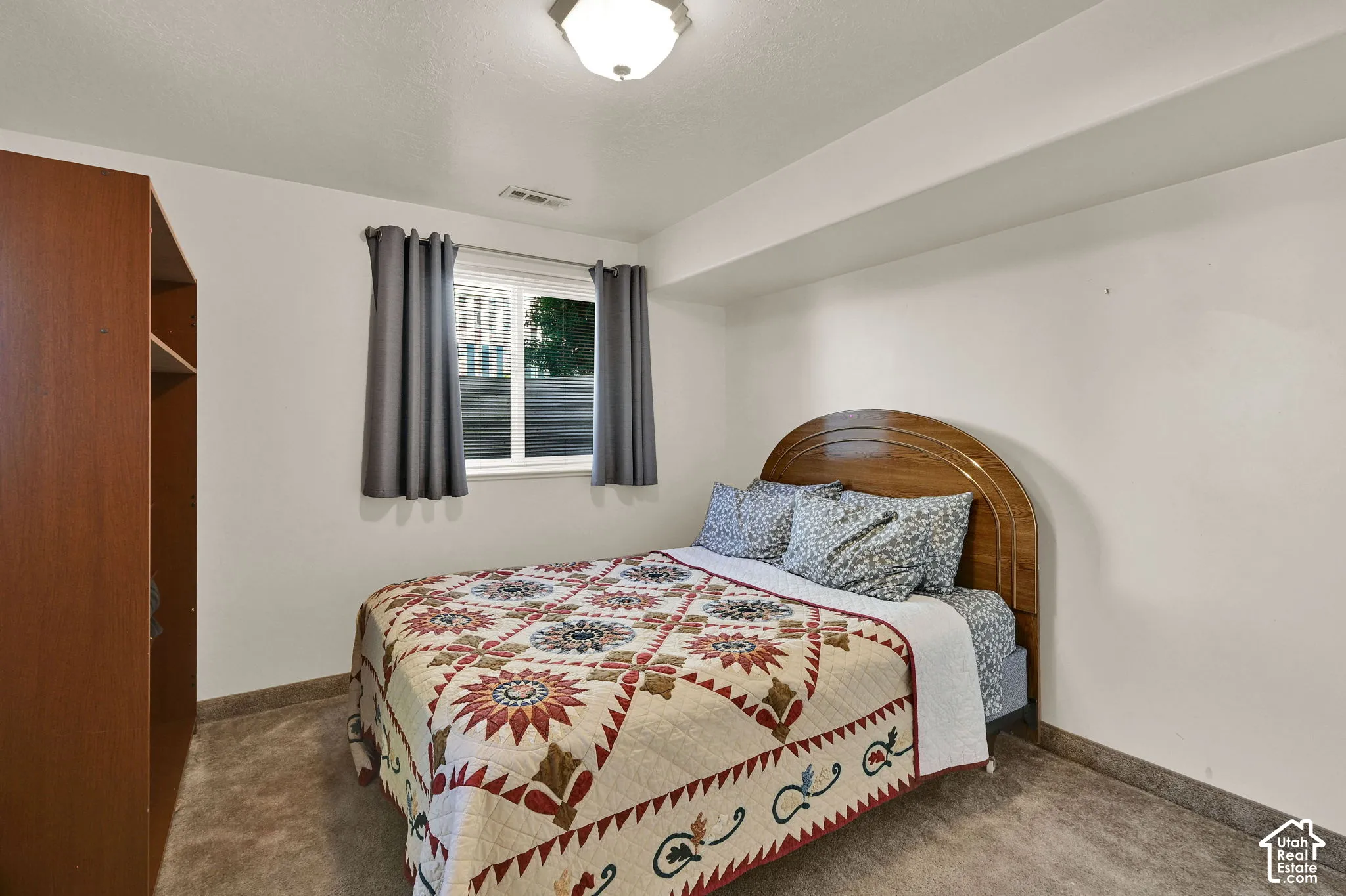 Recessed ceiling light fixture illuminating a neutral-toned room with a window, wood-finish headboard, and wood-finish open shelving unit