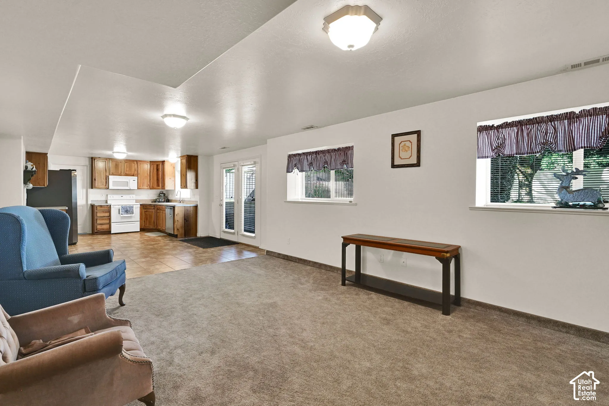 Carpeted living area with two windows, a kitchen featuring wood-finish cabinetry, a white range, and a white microwave, and French doors leading to an outdoor space