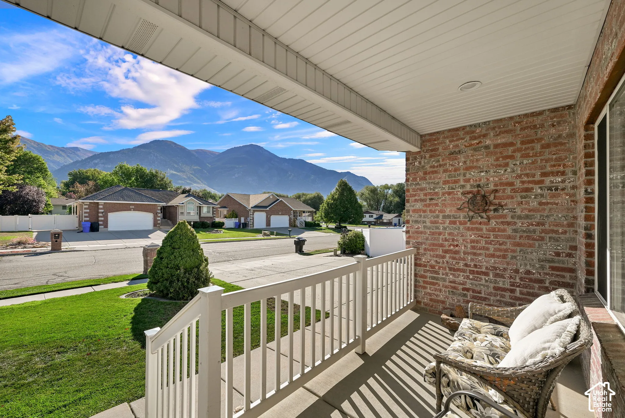 Covered front porch with a brick exterior, white railings, and a mountain backdrop