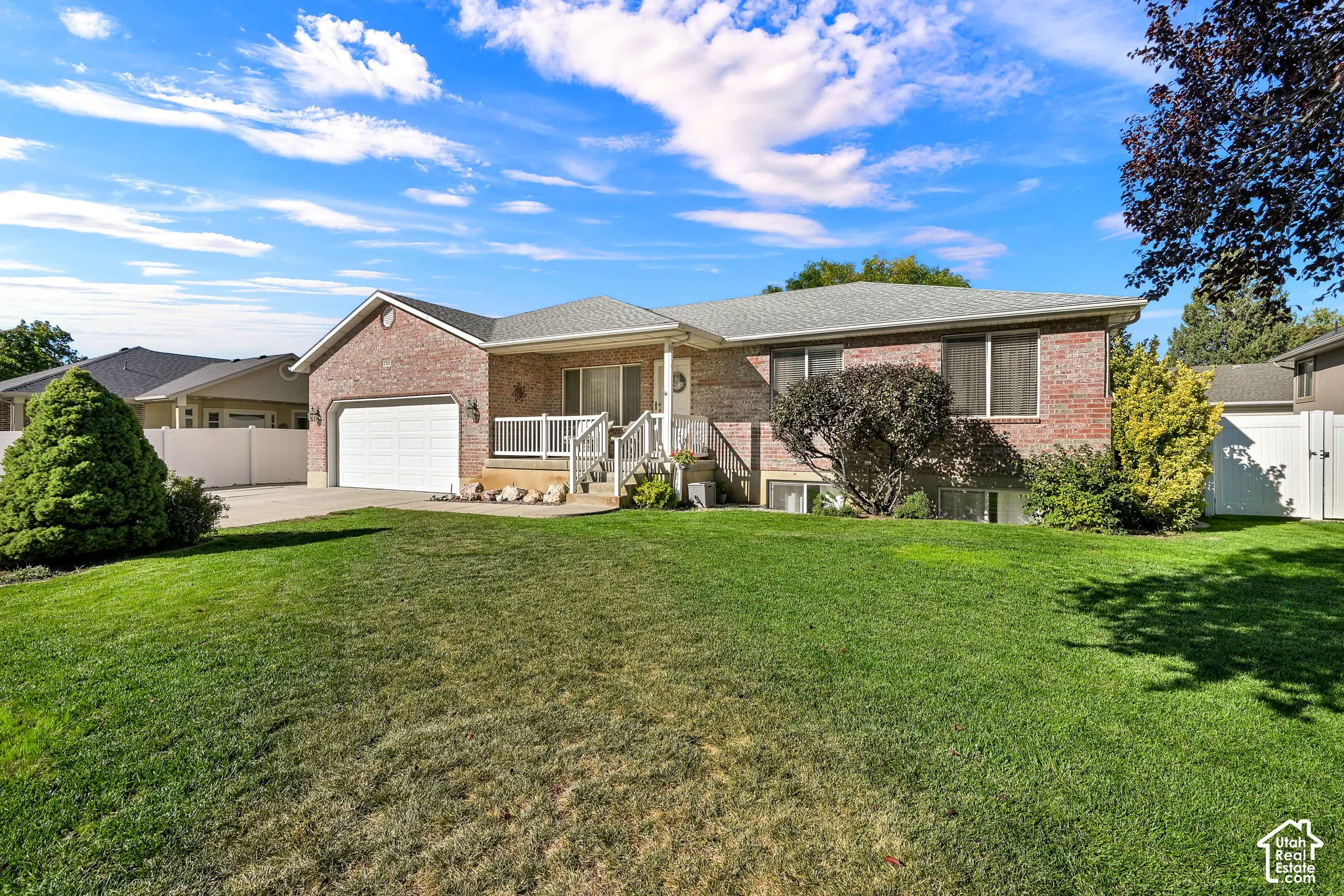 Brick exterior with a white garage door, front porch with white railing, and mature landscaping