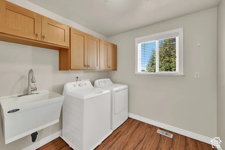 Laundry room featuring wood-finish flooring, a utility sink with a gooseneck faucet, light wood cabinetry, and a window with blinds