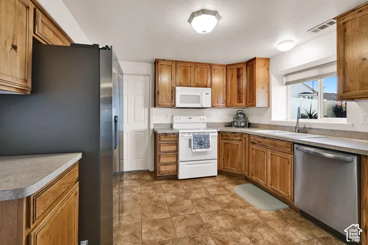 Wood cabinetry with stainless steel appliances, durable countertops, and tiled flooring