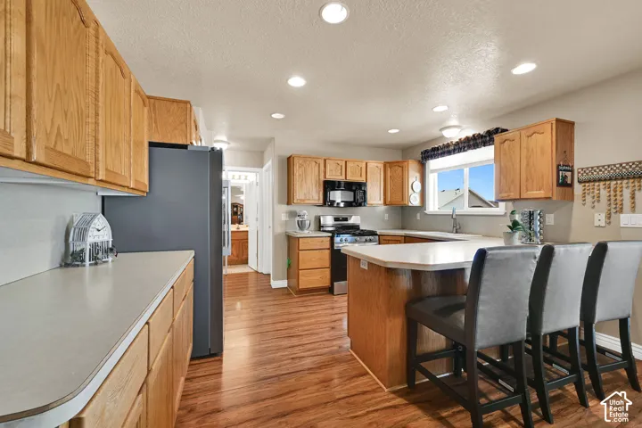 Kitchen featuring wood-finish flooring, recessed lighting, wood cabinetry, and an island with counter seating