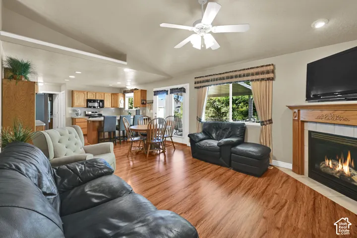 Wood-finish flooring throughout, vaulted ceiling with a ceiling fan, and a gas fireplace with a wood mantel