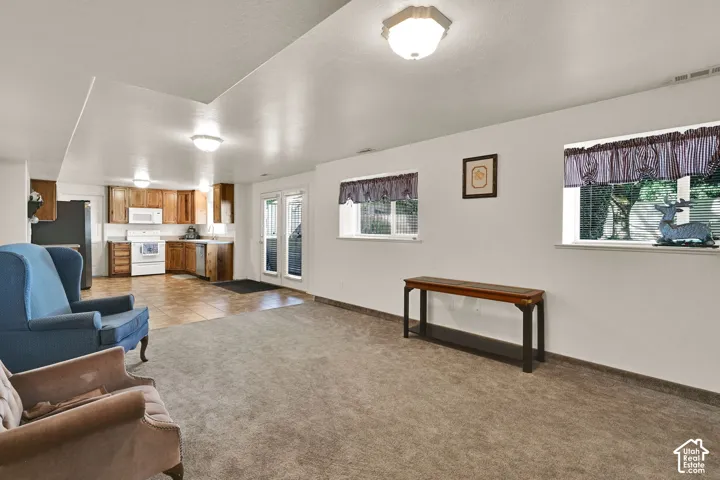 Carpeted living area with two windows, a kitchen featuring wood-finish cabinetry, a white range, and a white microwave, and French doors leading to an outdoor space