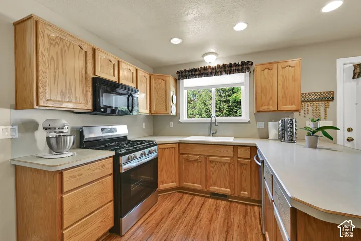 Kitchen featuring wood-finish cabinetry, light-toned countertops, stainless steel gas range, and an integrated microwave