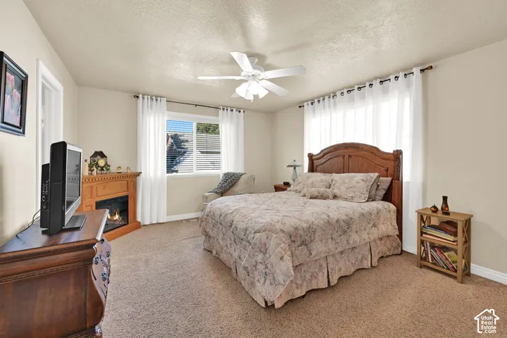 Recessed lighting, wood-finish fireplace surround, large window with blinds, ceiling fan, and carpeted flooring