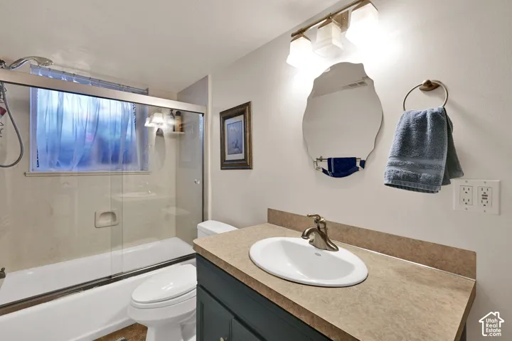 Bathroom featuring a vanity with an integrated sink, a built-in bathtub with a sliding glass enclosure, and an overhead light fixture