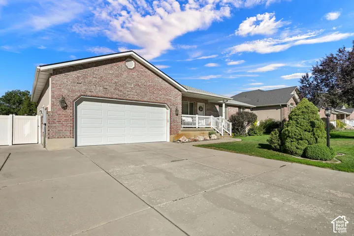 Brick veneer exterior, two-car garage, concrete driveway, white porch railings, and established landscaping