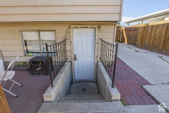 Red paver patio with concrete steps, wrought iron railing, and a side door entry