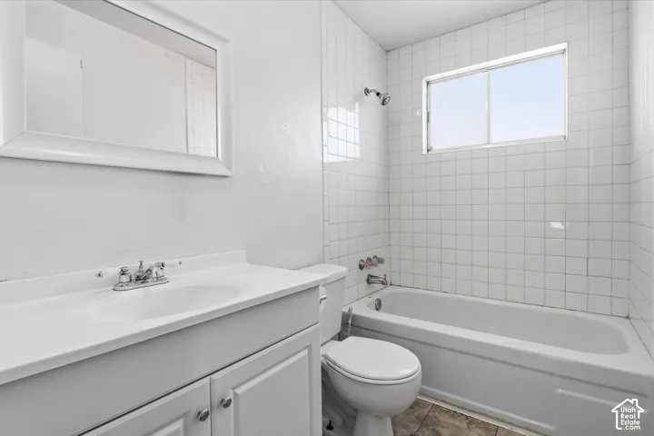 Bathroom featuring a single-sink vanity with cabinet storage, a framed mirror, a bathtub with an integrated shower, and white tile surround