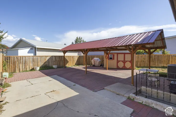Covered patio area with a red metal roof, brick paver flooring, and a wooden privacy fence
