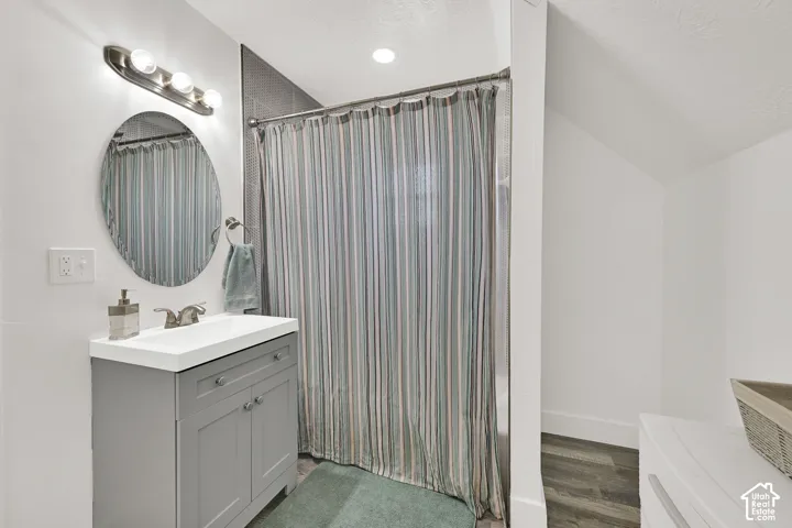 Vanity with a rectangular sink, wood-finish flooring, and a tiled shower surround