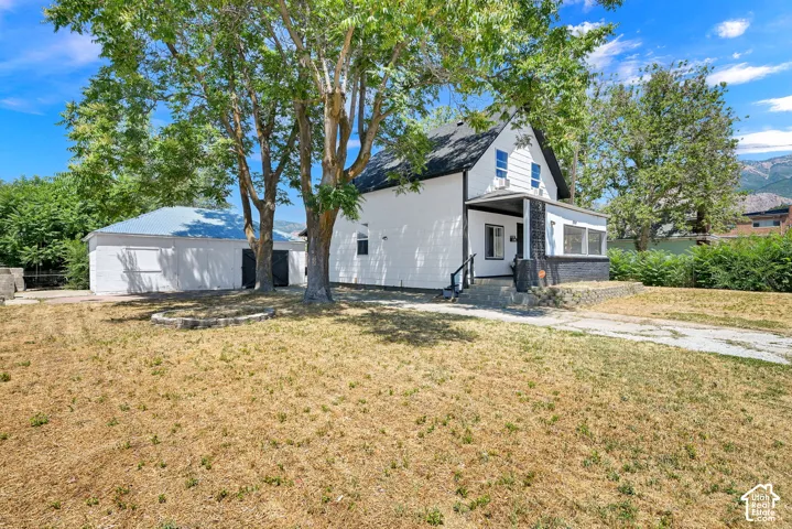 White exterior with black trim, covered porch, and a detached structure with a blue metal roof
