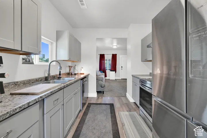 Kitchen featuring stainless steel appliances, light gray cabinetry, a double basin sink with a high-arc faucet, and wood-finish flooring