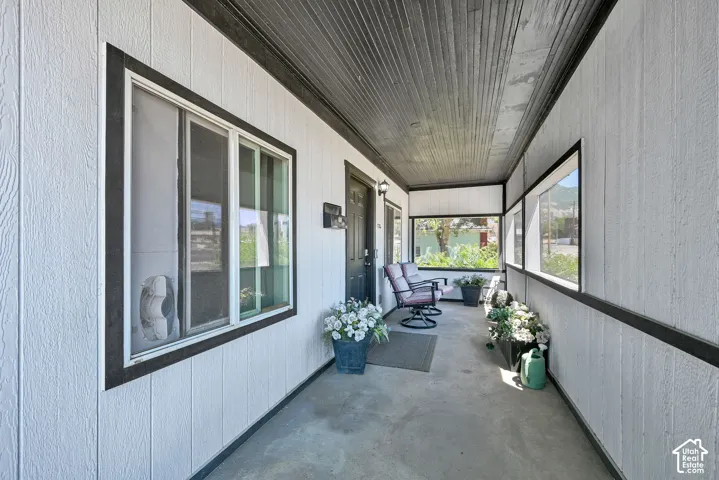 Covered porch with white vertical panel siding, dark trim, multiple windows, and dark ceiling panels