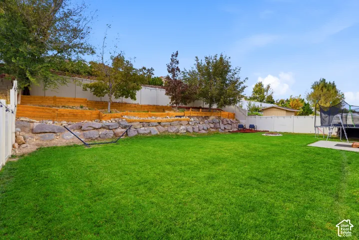 Expansive backyard featuring a meticulously manicured lawn, mature landscaping with mixed deciduous and evergreen trees, and a decorative stone retaining wall