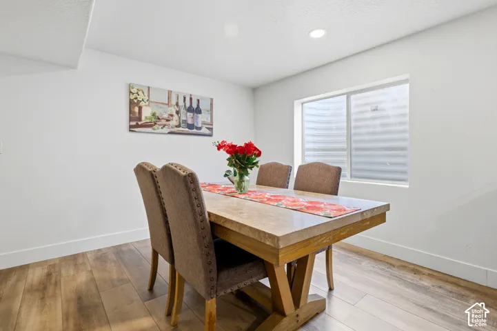 Dining space featuring a wood-finish table with angled legs, upholstered dining chairs with nailhead trim, recessed ceiling lighting, and large sliding glass doors with horizontal blinds providing natural light and access to adjacent outdoor space