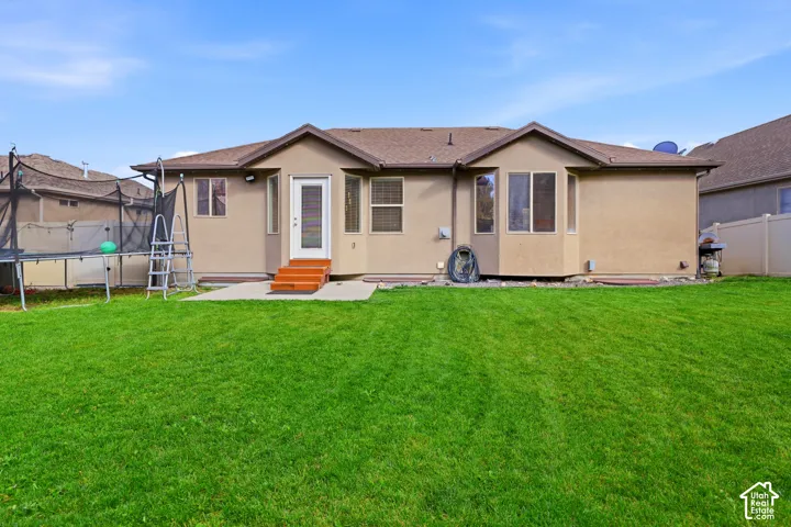Expansive green lawn, stucco exterior, multiple windows, rear entry door with steps, and a bay window feature