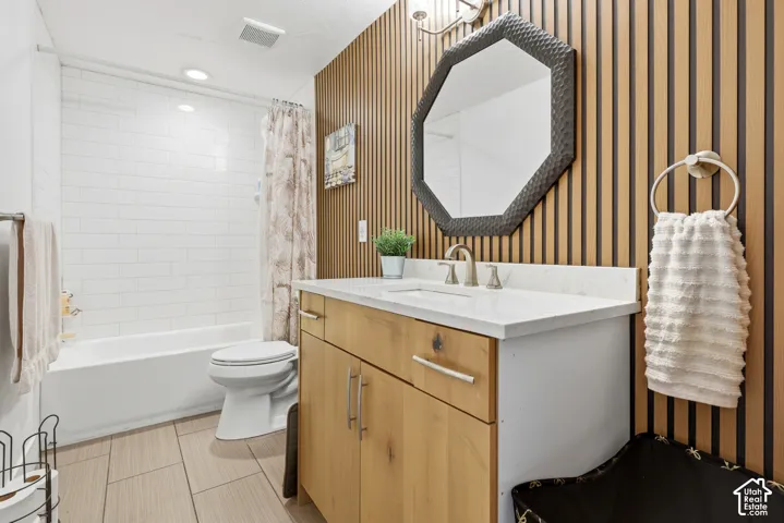 Bathroom featuring a wood-finish accent wall, octagon-shaped mirror, wood-finish vanity with a light-colored countertop, white subway tile shower surround, and tile flooring