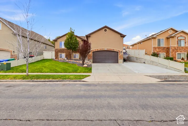 Charming two-story residence featuring a stucco exterior with peaked roofline, two-car garage with dark finish doors, and manicured front lawn with mature landscaping