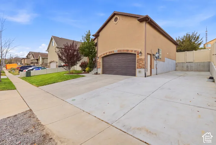 Spacious driveway with concrete surface leading to a two-car garage featuring a dark finish door and stone accents