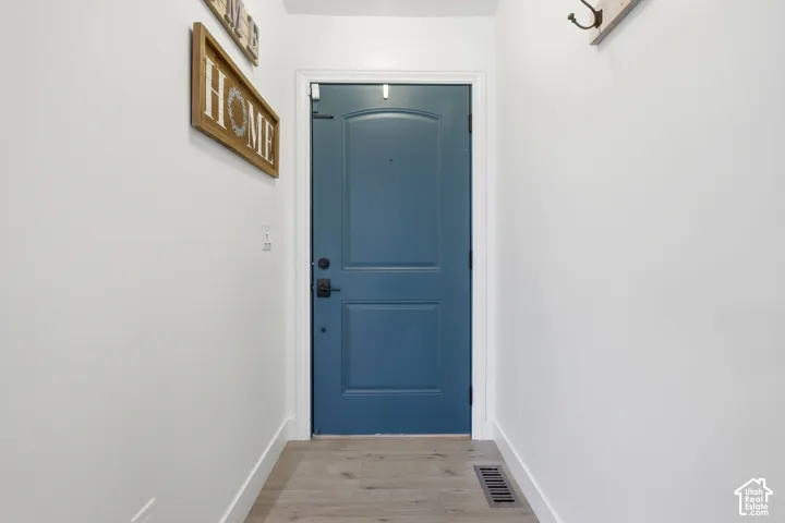 Welcoming entryway featuring a striking blue six-panel door with oil-rubbed bronze hardware, white trim, and wood-finish flooring throughout the corridor