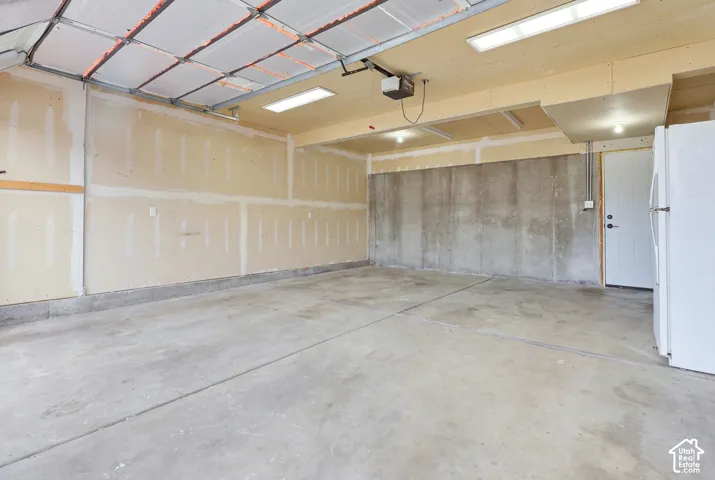 Spacious garage featuring polished concrete flooring, insulated paneled walls, recessed lighting throughout, and an attached service door for convenient access