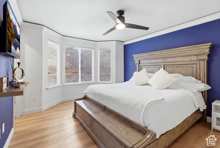 Primary Bedroom featuring hardwood flooring, a wood-finish bed frame with decorative molding, crisp white bedding, and abundant natural light from multi-panel bay windows with plantation shutters