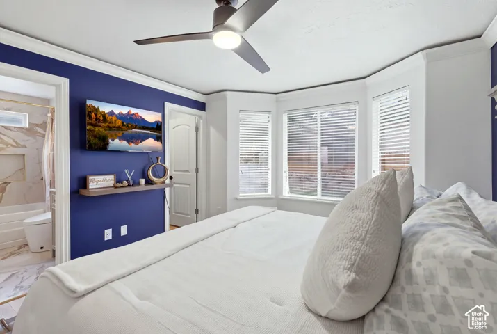 Recessed bay window with blinds, ceiling fan, crown molding, and an attached bathroom featuring a built-in tub with a niche