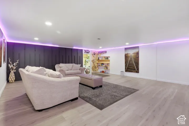 Recessed lighting and perimeter strip lighting illuminate a spacious room featuring plank flooring, a dark accent wall, and built-in shelving