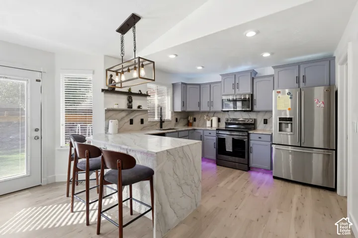 Contemporary kitchen featuring light wood-finish flooring, an oversized island with a waterfall counter, light gray cabinetry, stainless steel appliances, and recessed lighting