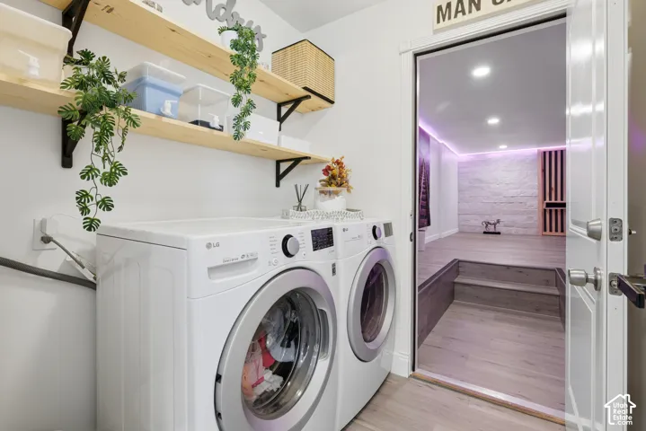 Modern laundry room featuring dual front-load washers and dryers with white finish, floating wood shelving with decorative planters, recessed ceiling lighting, and direct access to a spa-inspired bathroom retreat with purple ambient lighting and tile fini