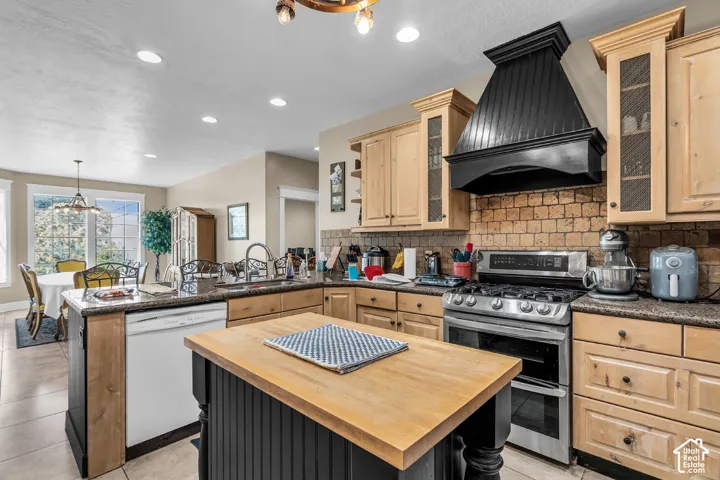 Kitchen featuring a freestanding central island with a wood-finish countertop, light wood cabinetry, a dark tile backsplash, stainless steel appliances, and recessed lighting