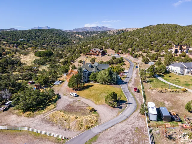 Spacious lot with a white three-rail fence, paved drive, and surrounding natural landscaping