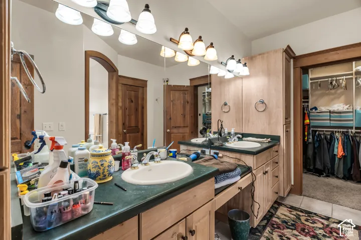 Double vanity with integrated sinks, green countertops, wood-finish cabinetry, and overhead lighting fixtures