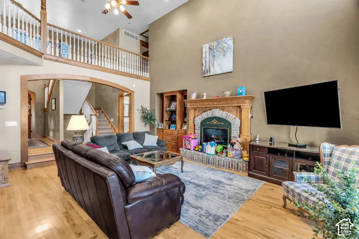 Hardwood flooring, two-story ceiling, stone-surround fireplace with wood mantel, open architectural archway, and ceiling fan