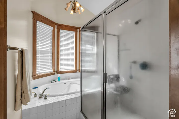 Jetted soaking tub with tile surround, wood-trimmed bay windows, and frosted glass shower enclosure