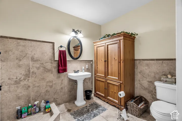 Pedestal sink, wall-mounted oval mirror, vanity lighting fixture, toilet, and wood storage cabinet