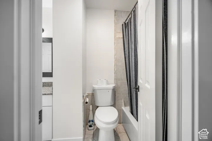 White toilet with a tiled accent wall and tub shower combination