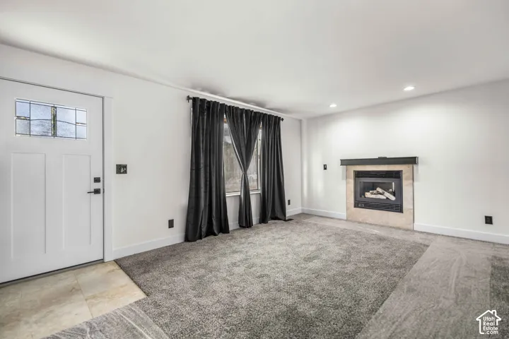 Entry foyer with ceramic tile flooring, a gas fireplace with a stone surround, recessed lighting, and a white paneled door with leaded glass accents