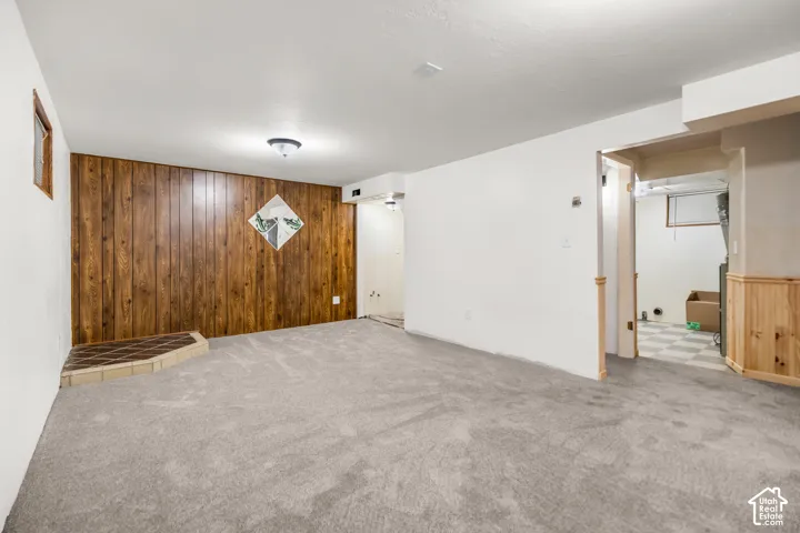 Carpeted flooring, wood-paneled accent wall, overhead lighting, and an adjacent utility area