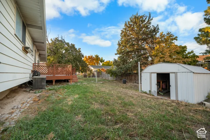 Rear yard featuring a wood deck, a metal storage shed, and mature trees